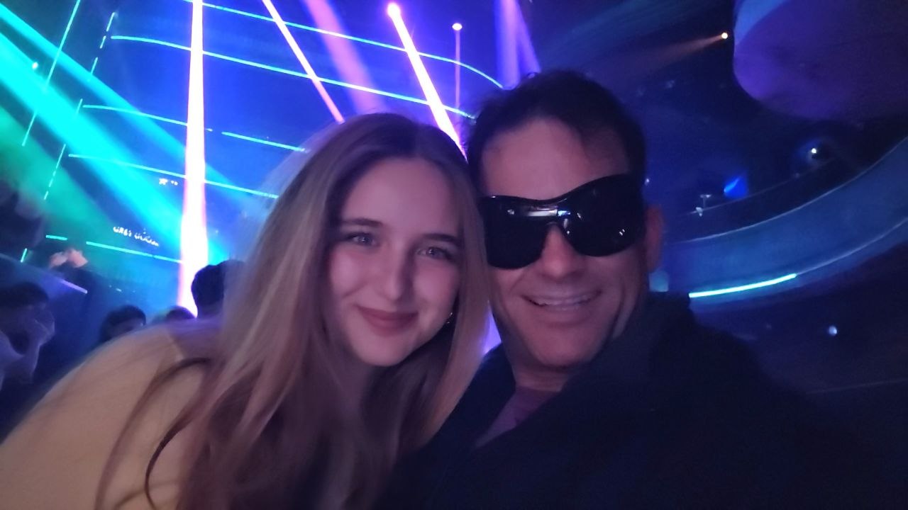 Gabriel and Ximena smiling together in a nightlife setting with colorful lights.