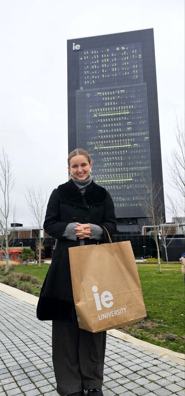 Ximena smiling in front of an IE University building while holding an IE University bag.
